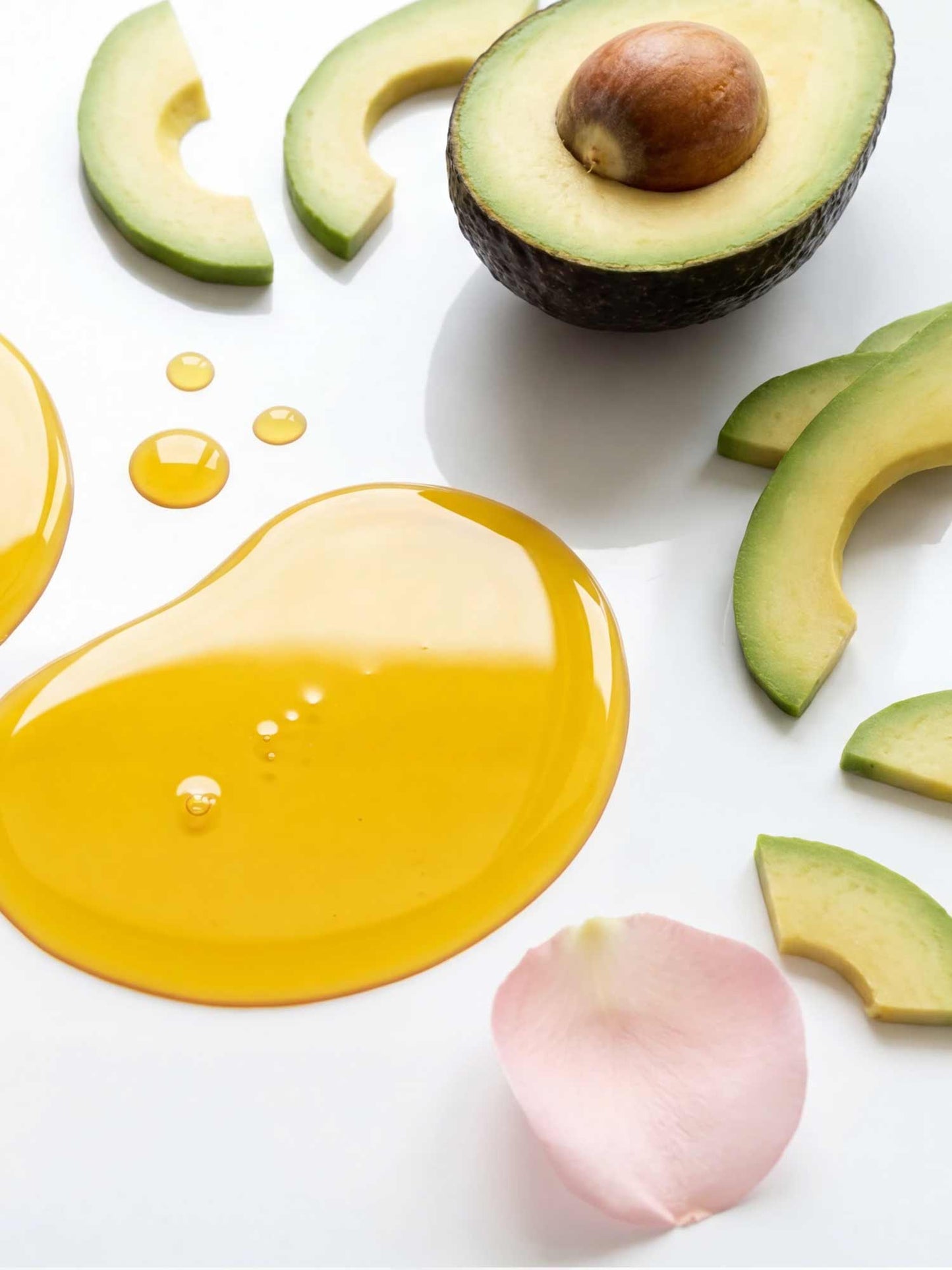 Avocado slices and a whole avocado with a droplet of oil on a white background